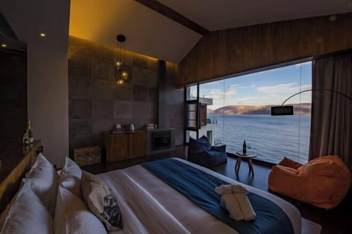 A modern hotel room with a large bed, a small seating area, a television, and a view of the sea.