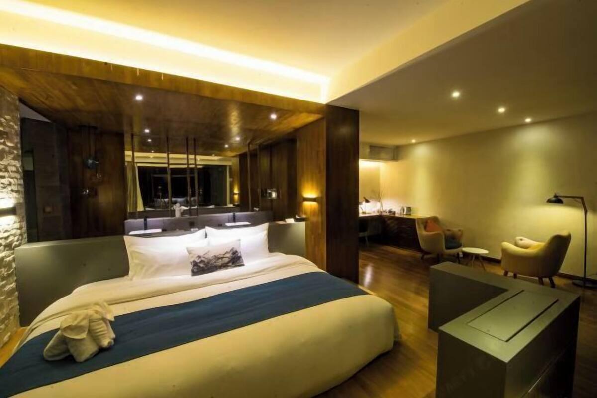 A modern hotel room with a large bed, a sitting area with a desk, and a mirror.
