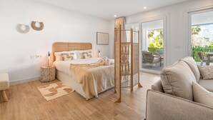 Een moderne slaapkamer met een houten hoofdeinde, een groot bed met witte lakens, een nachtkastje met een lamp, en uitzicht op de omgeving door een glazen deur.