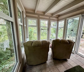 Una habitación con dos sillones mullidos, ventanas amplias y vistas al verdor exterior.