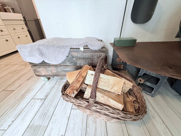 Une pièce rustique avec un banc en bois, un panier en osier rempli de bois de chauffage et une commode à tiroirs.