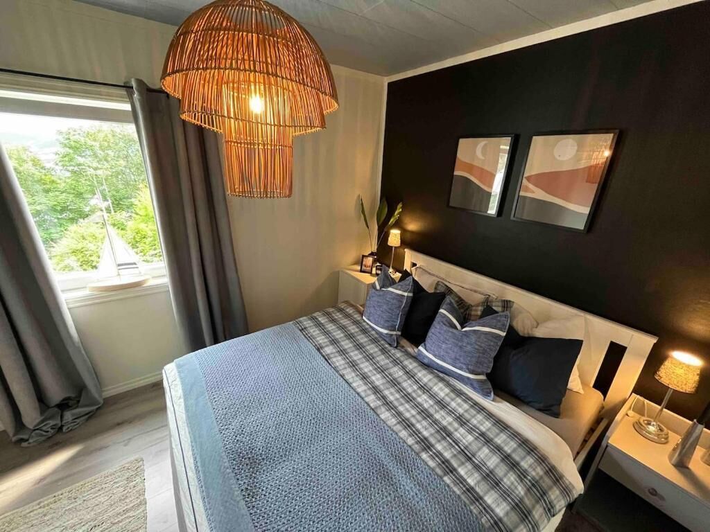 Un dormitorio con una cama grande, una mesita de noche con lámpara, una lámpara colgante y dos obras de arte en la pared.