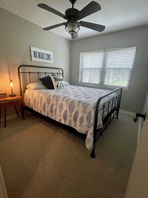 A bedroom with a bed, a nightstand, a wall clock, a ceiling fan, and a window with blinds. - Charming and cozy river home (Palatka)
