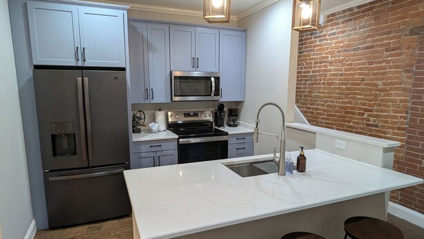 Una cocina moderna con armarios grises, electrodomésticos de acero inoxidable, una isla grande con taburetes y una pared decorativa de ladrillo.