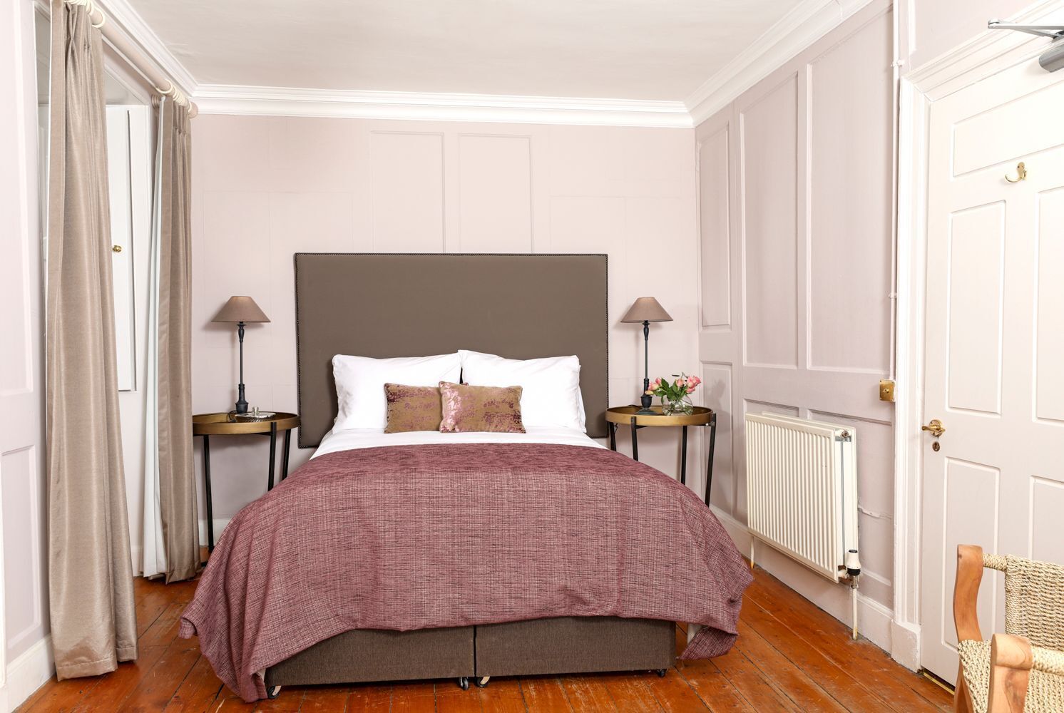A bedroom with a large bed, two bedside tables, a radiator, and a door.