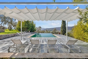 Un espace aménagé au bord de la piscine, avec une pergola, des chaises longues et une vue sur le paysage.