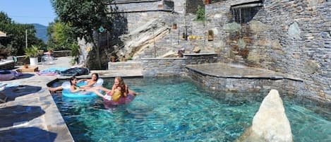 Una piscina con agua cristalina, paredes de piedra y una estructura de piedra en el centro.