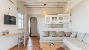 Una sala de estar moderna con un sofá, dos mesas redondas de madera, un televisor montado en la pared y un ventanal con vistas.