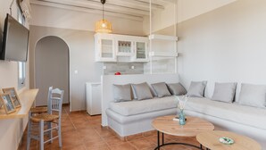 Una sala moderna con sofá, una mesa de comedor, una silla, televisor y una cocina con armarios.