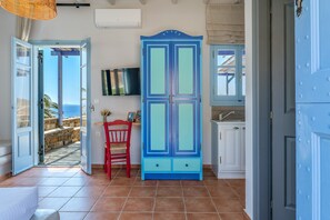 An open door leading to a balcony with a stone wall, a red chair, a blue cabinet, and a TV mounted on the wall. - Apartment 'Unit 1' with Sea View, Wi-Fi and Air Conditioning (Tinos)