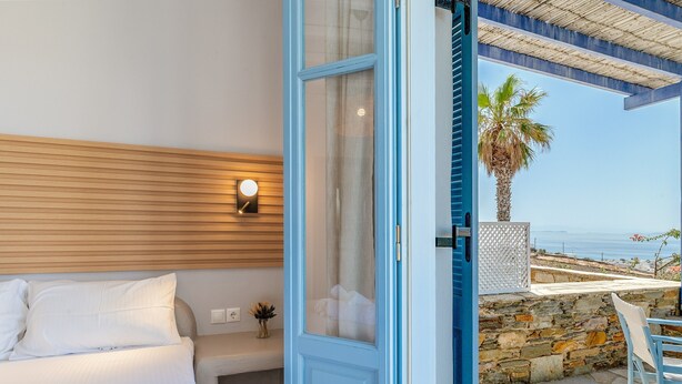 A bedroom with a bed, a nightstand, a wall-mounted light, and a view of the ocean through an open door. - Apartment 'Unit 2' with Sea View, Wi-Fi and Air Conditioning (Tinos)