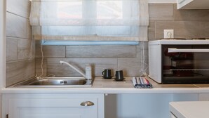 A kitchen with a sink, a microwave, and a window with a blind. - Apartment 'Unit 2' with Sea View, Wi-Fi and Air Conditioning (Tinos)