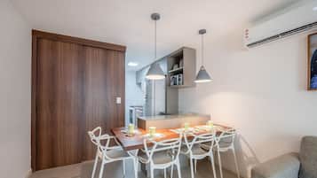 A modern kitchen with a dining area, white chairs, pendant lights, and a grey sofa.