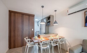 Cozinha moderna com área de refeições, cadeiras brancas, luminárias pendentes e sofá cinza.