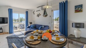 A modern living room with a dining area, featuring a large table set for breakfast, a blue sofa, and a TV on the wall. - #315 Apartamento Turístico Balaia by Home Holidays (Albufeira)
