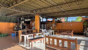 Un patio al aire libre con mobiliario de madera, una estación de parrilla y una zona de estar cubierta.