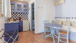 A compact kitchen with a blue table and chairs, a small refrigerator, and a blue cabinet with glass doors. - Apartment '5' with Sea View, Wi-Fi and Air Conditioning (Tinos)