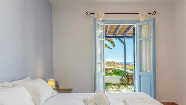 A bedroom with a bed, towels, a nightstand, and a view of a garden through an open door.