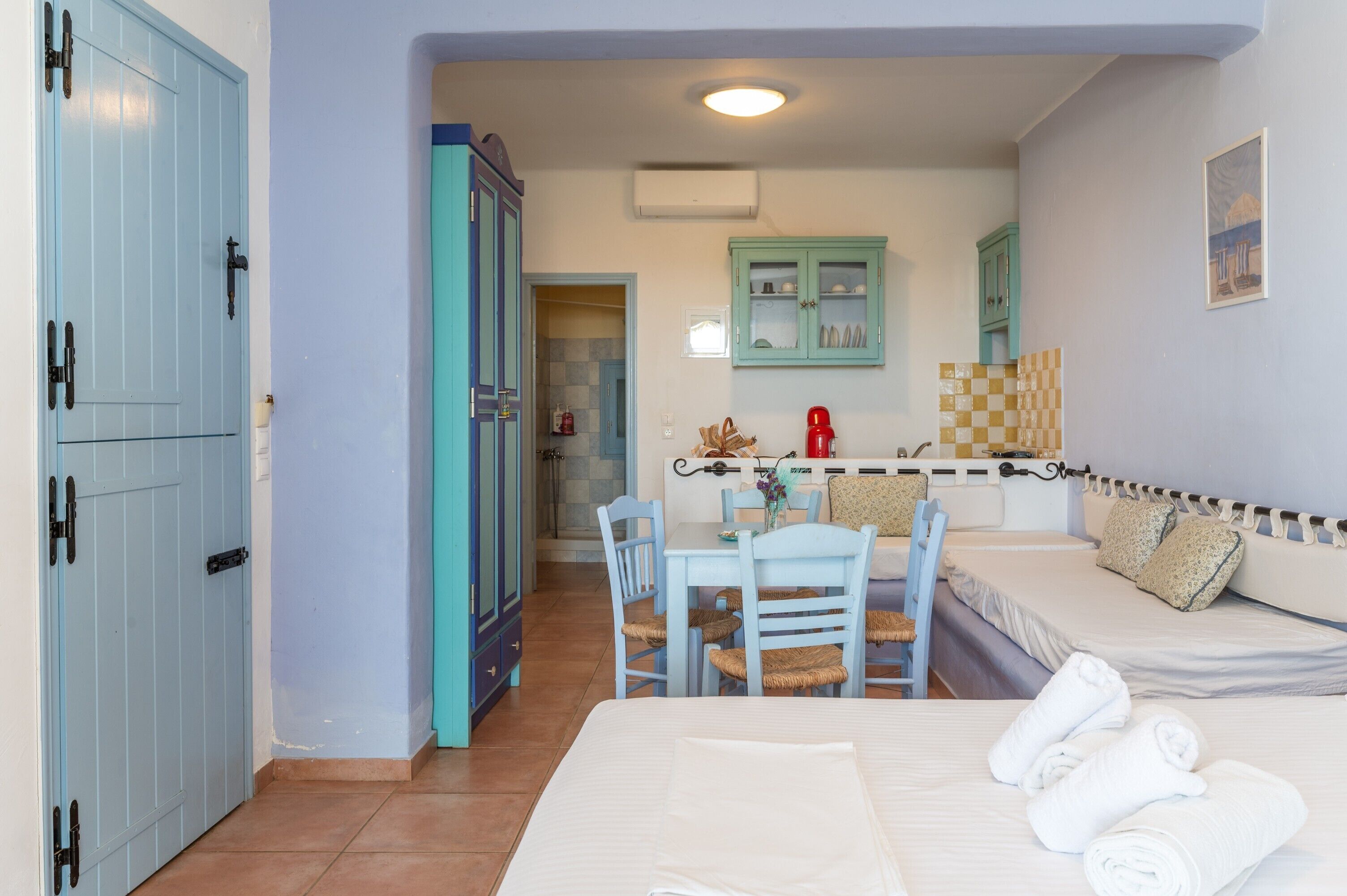 A room with a bed, a dining table with chairs, a kitchenette, and a bathroom with a shower.