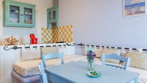 A room with a checkered wall, a dining table with chairs, a red kettle, and teal cabinets.