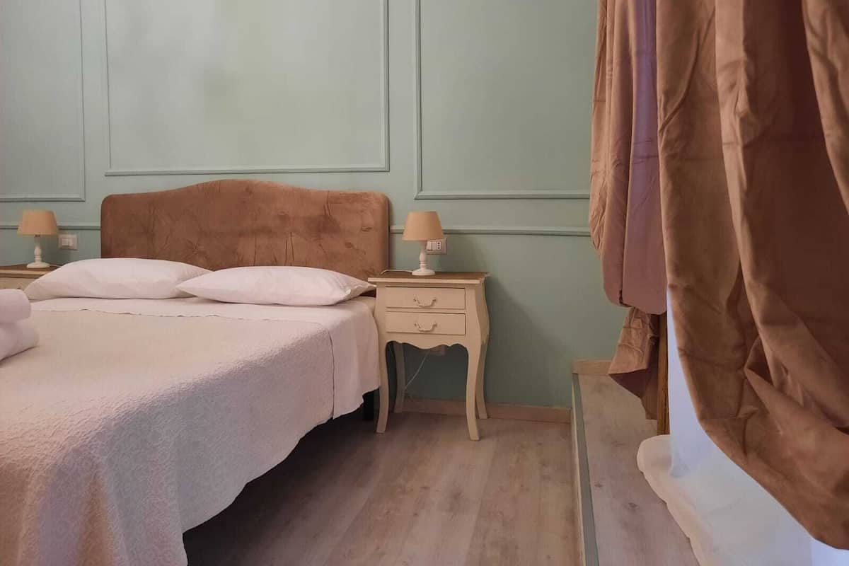 A bedroom with a bed, two bedside tables, a nightstand, and a curtain.