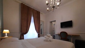 Una habitación de hotel con una cama grande, un escritorio con silla, televisión y un candelabro.