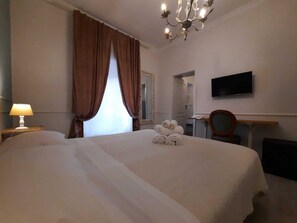 A hotel room with a large bed, a desk with a chair, a television, and a chandelier. - Urbana collection guest house (Rome)