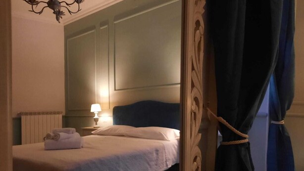 A neatly made bed with a white comforter and pillows, a bedside lamp, and a rolled towel on the nightstand. - Urbana collection guest house (Rome)