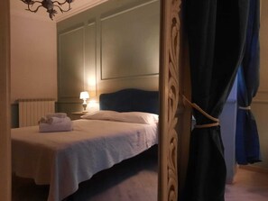 A neatly made bed with a white comforter and pillows, a bedside lamp, and a rolled towel on the nightstand. - Urbana collection guest house (Rome)
