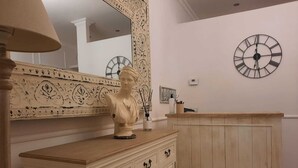 A room with a wooden cabinet, a bust sculpture on top, a large mirror with ornate designs, and a wall clock. - Urbana collection guest house (Rome)