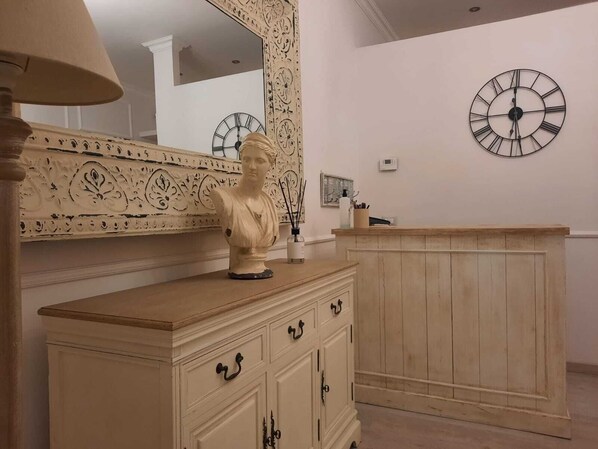 A room with a wooden cabinet, a bust sculpture on top, a large mirror with ornate designs, and a wall clock. - Urbana collection guest house (Rome)