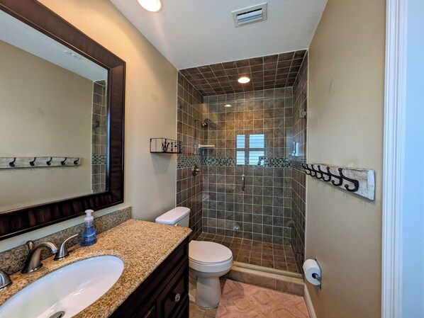 A bathroom with a sink, mirror, toilet, and shower area. - Entire home in Cocoa Beach, Florida. 6 guests, 4 bedrooms, 5 beds, 2 baths (Cocoa Beach)