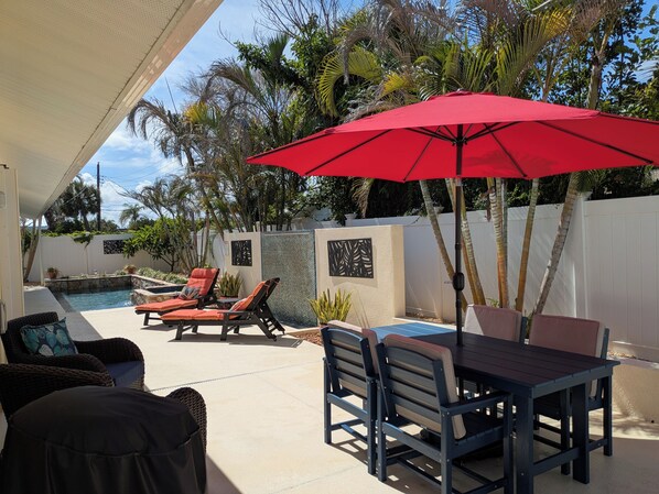 A poolside area with lounge chairs, a table, and a red umbrella.