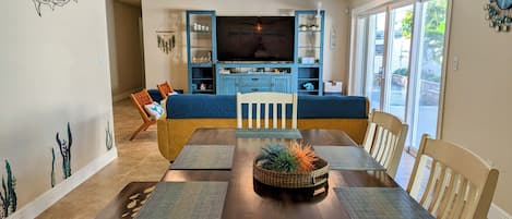 A dining area with a wooden table, blue cushioned seating, and a TV in the background.
