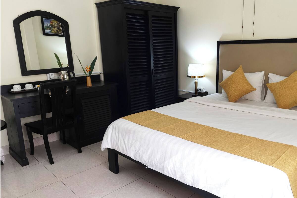 Une chambre d’hôtel comprenant un lit, un bureau, une armoire et une table de chevet avec une lampe.