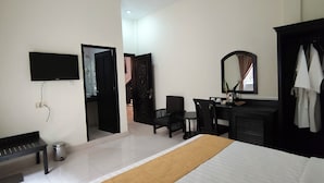 Een hotelkamer met een bed, een bureau met spiegel, een aan de muur bevestigde televisie, een bankje en een prullenbak.