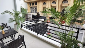 Een balkon met een tafel en stoelen, plantenbakken en uitzicht op een gebouw met klassieke architectuur.