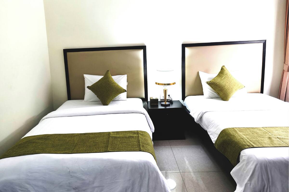 Une chambre d’hôtel avec deux lits simples, chacun recouvert d’un plaid vert et agrémenté d’un oreiller blanc.
