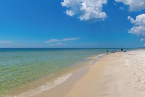 A beach with clear turquoise water, sandy shore, and a few people.