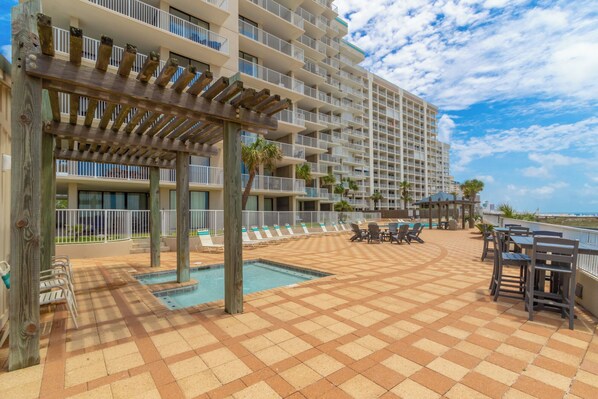 A resort pool area with a pergola, lounge chairs, and a view of the ocean.