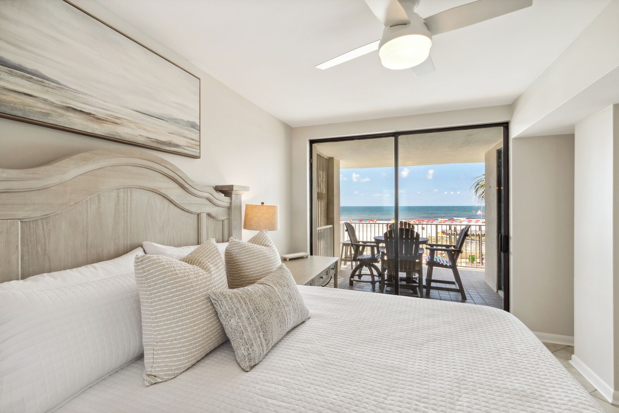 Ein Schlafzimmer mit einem großen Bett, einem Deckenventilator und Blick auf den Strand durch eine Schiebetür.