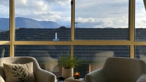 Una habitación con un ventanal grande con vistas a un paisaje urbano, una chimenea y dos sillones.