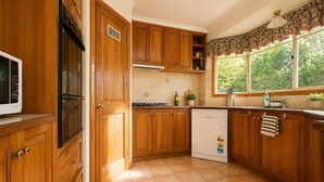 Una cocina con armarios de madera, microondas, lavavajillas y ventana con vistas a zonas verdes.