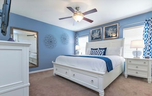 Un dormitorio con cama blanca, ventilador de techo, mesita de noche, cómoda y decoración mural.
