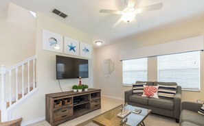 Una sala de estar con televisor de pantalla plana, ventilador de techo, sofá y mesa de centro.