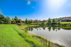 A serene outdoor setting with a pond, grassy areas, and buildings in the background.