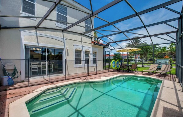 Uma área de piscina com piscina azul cristalina, rodeada por um revestimento de vidro, e um terraço com mobiliário de exterior.