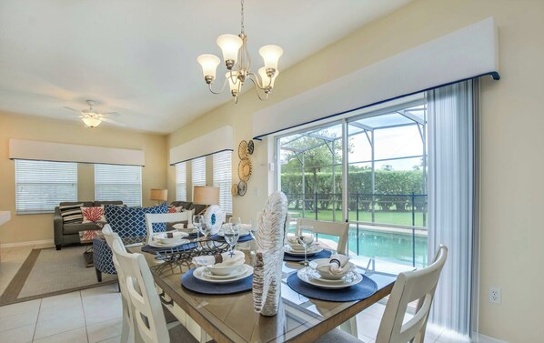 Comedor con una mesa dispuesta para cuatro, un candelabro y vistas a una piscina.