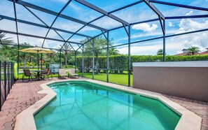 Una piscina con cerramiento de vidrio, rodeada por un patio con sillas y una sombrilla.