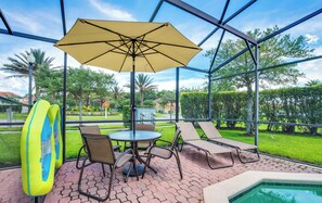Un patio exterior con una mesa, sillas, una sombrilla y una piscina.